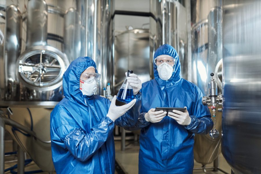 Two workers doing tests at chemical factory and wearing protective suits Waist up portrait of two workers doing tests at chemical factory and wearing protective suits